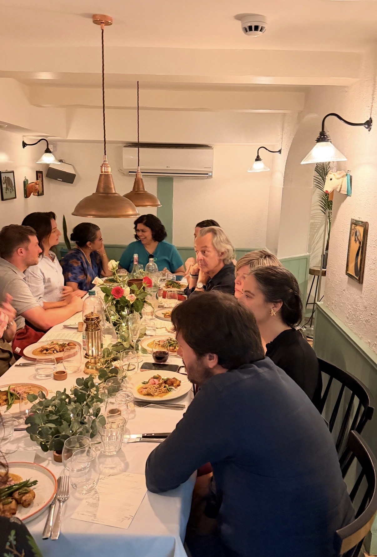 Guests sharing plated dishes around a flower-filled supper-club table