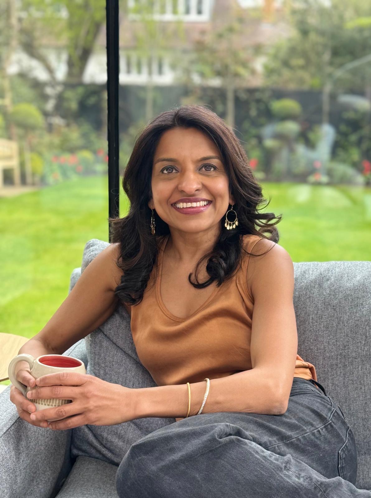 Sabina smiling with a mug, seated beside a garden window