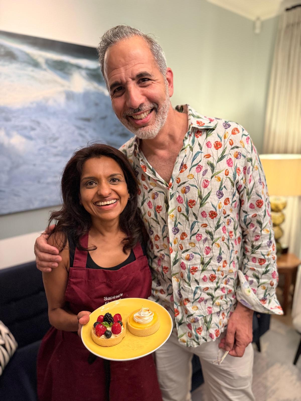 Sabina holding a plate of fruit and lemon tarts beside a guest at a celebration