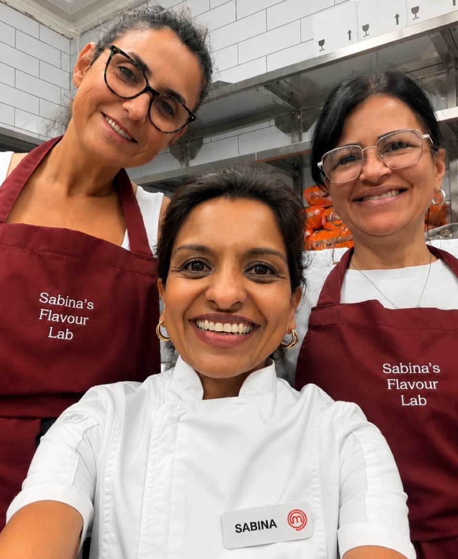 Sabina in her chef whites with two members of the Flavour Lab team in burgundy aprons, in a kitchen before service