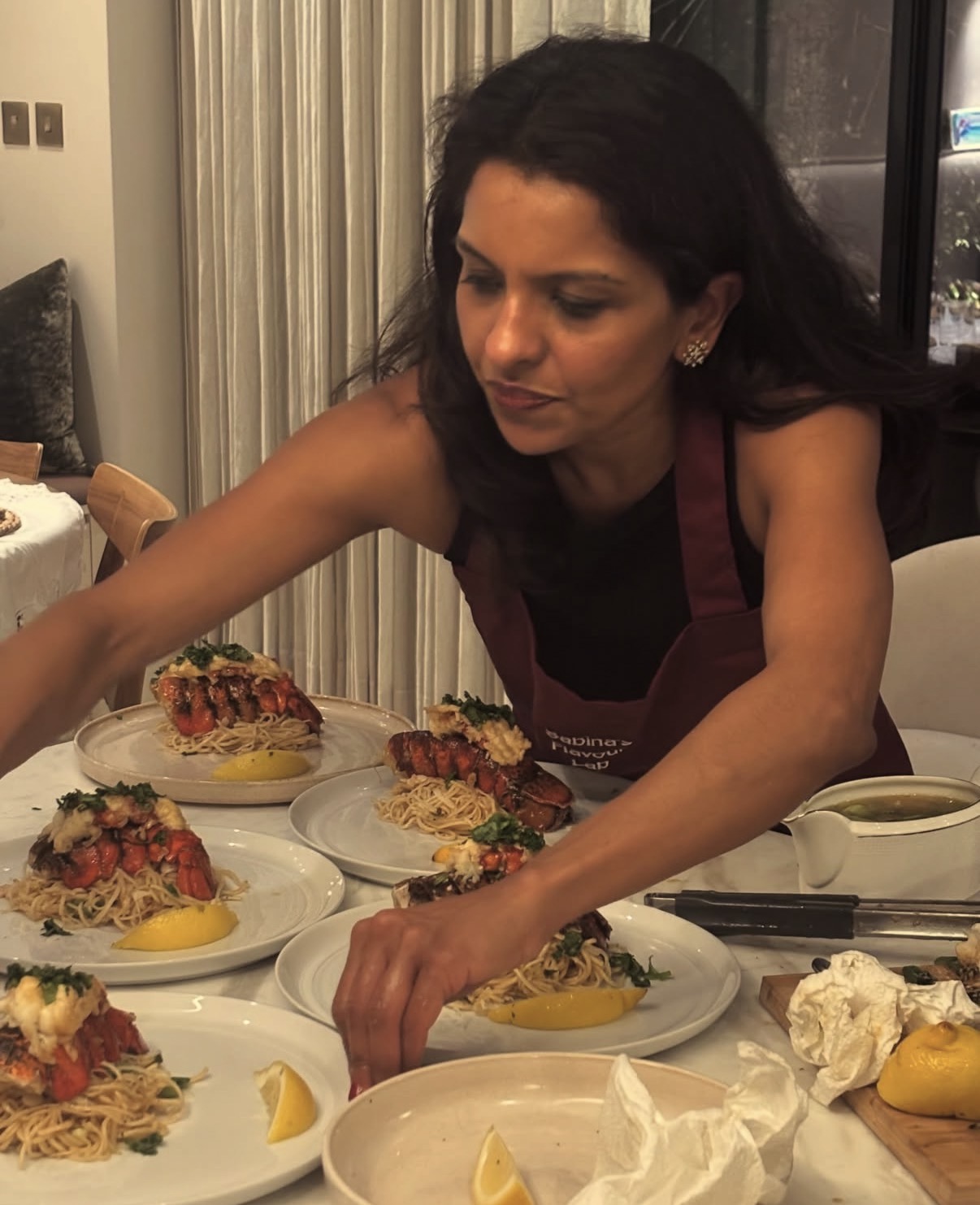 Sabina in her burgundy Flavour Lab apron plating lobster pasta across a marble table