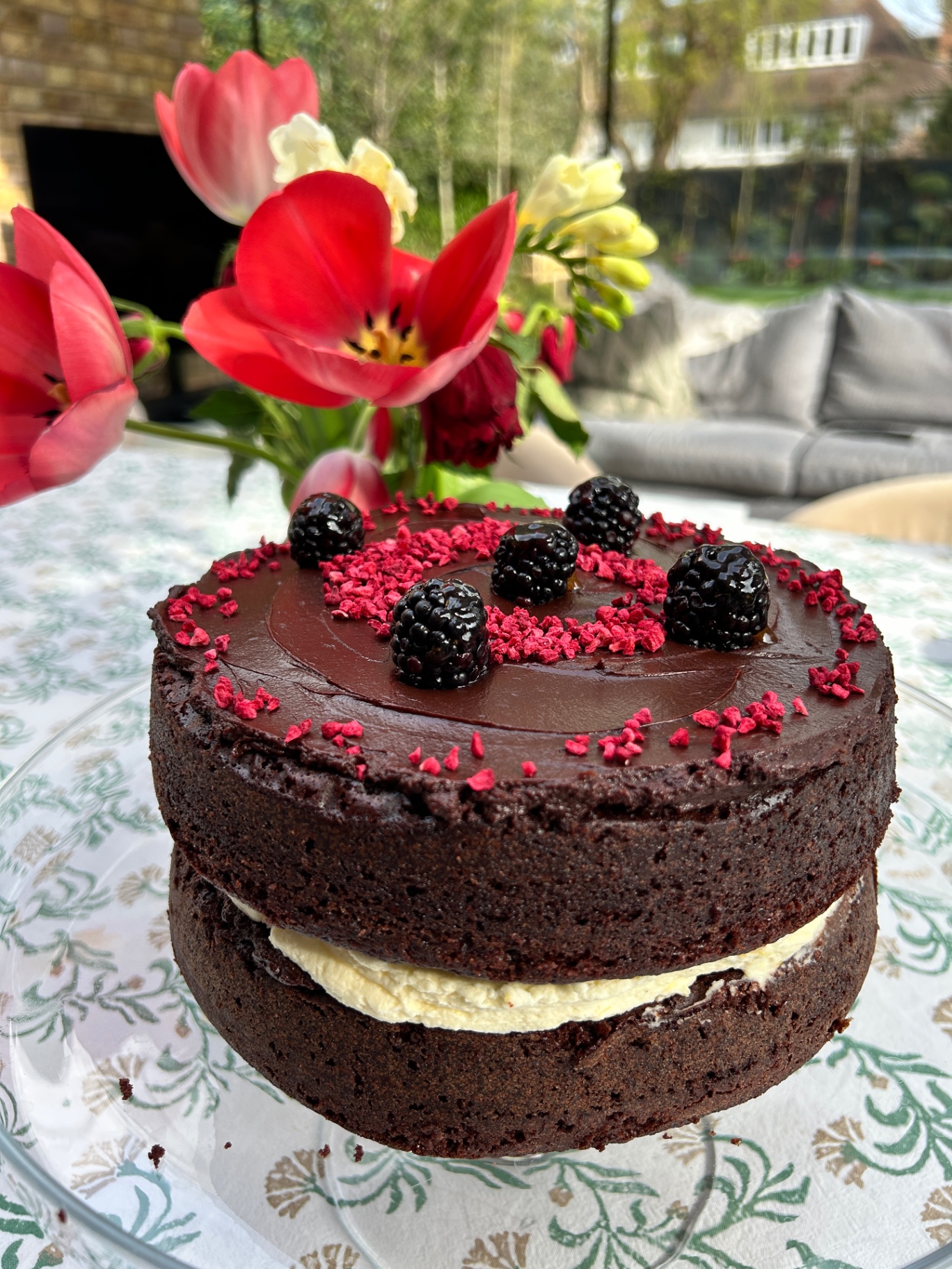 Chocolate layer cake with cream, blackberries and raspberry pieces beside fresh tulips