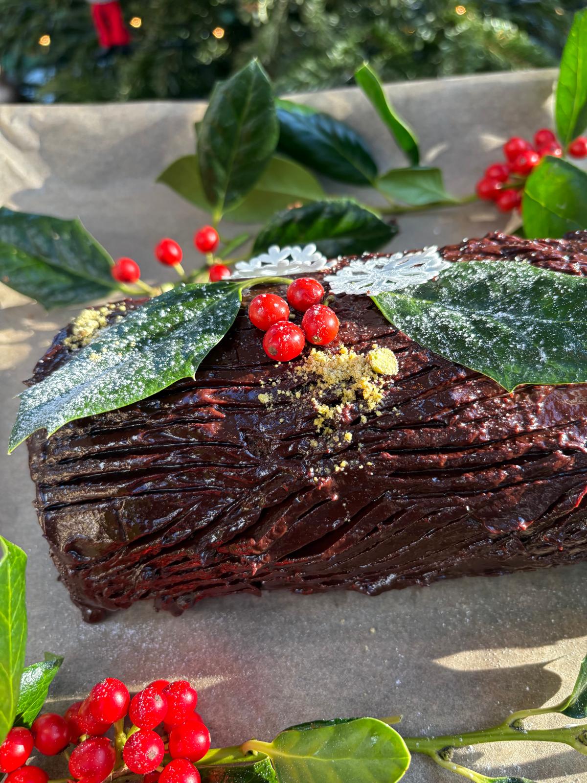 Chocolate Yule log decorated with holly, red berries and a dusting of sugar